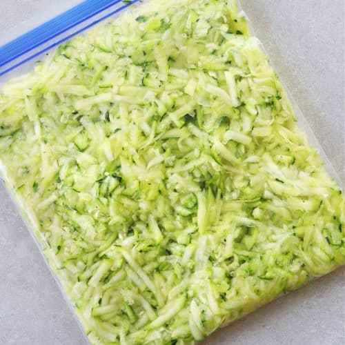 Shredded zucchini in a freezer bag on a gray background.