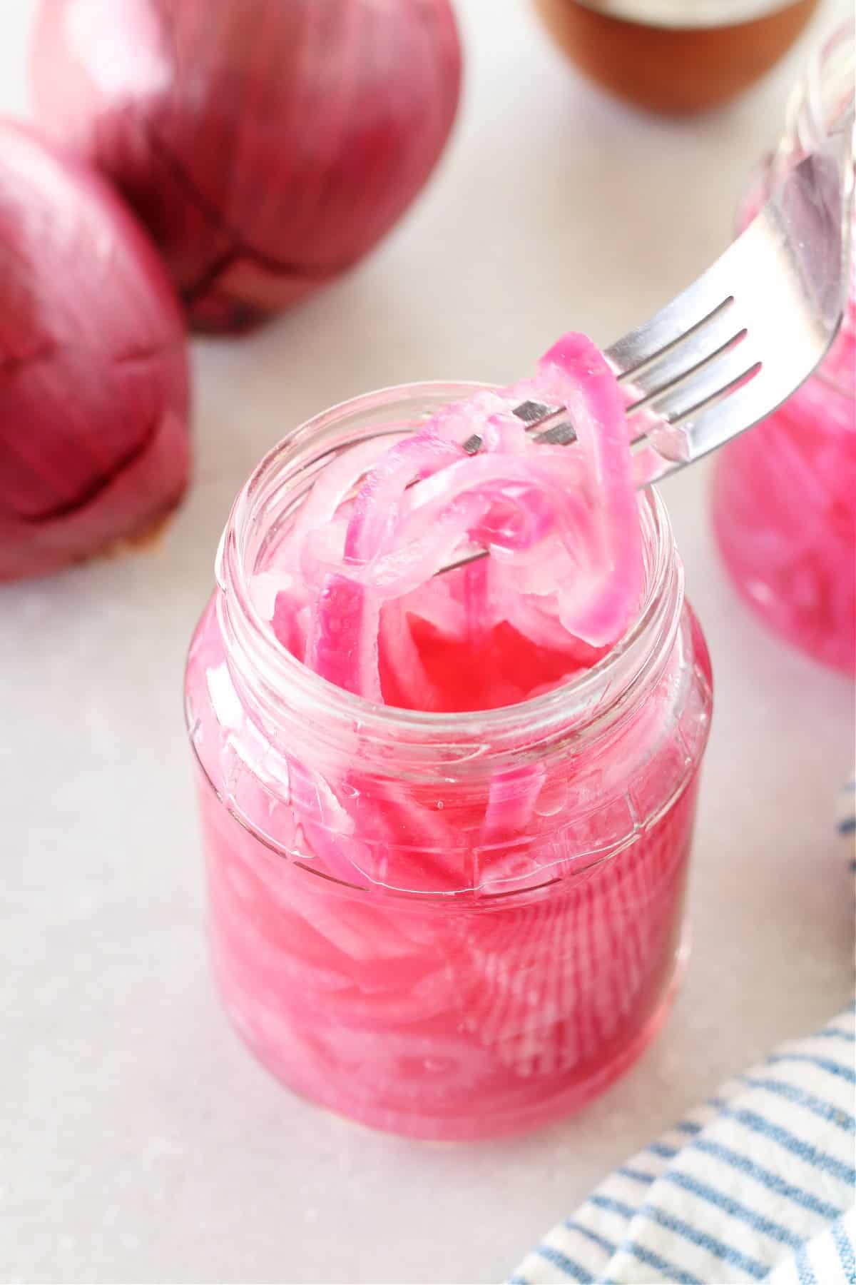 Pickled red onions in a jar and lifted on a fork.