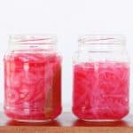 Two jars of pickled red onions on a wooden board.