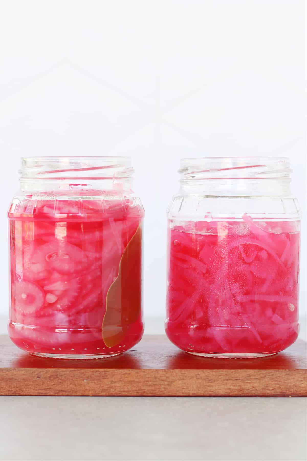 Two jars of pickled red onions on a wooden board.