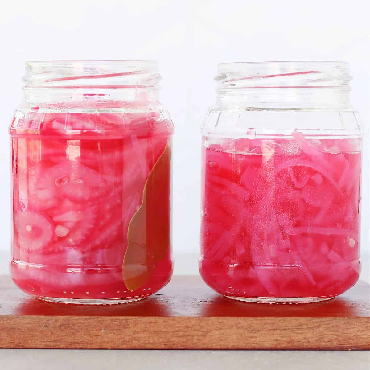Two jars with pickled red onions on a cutting board.