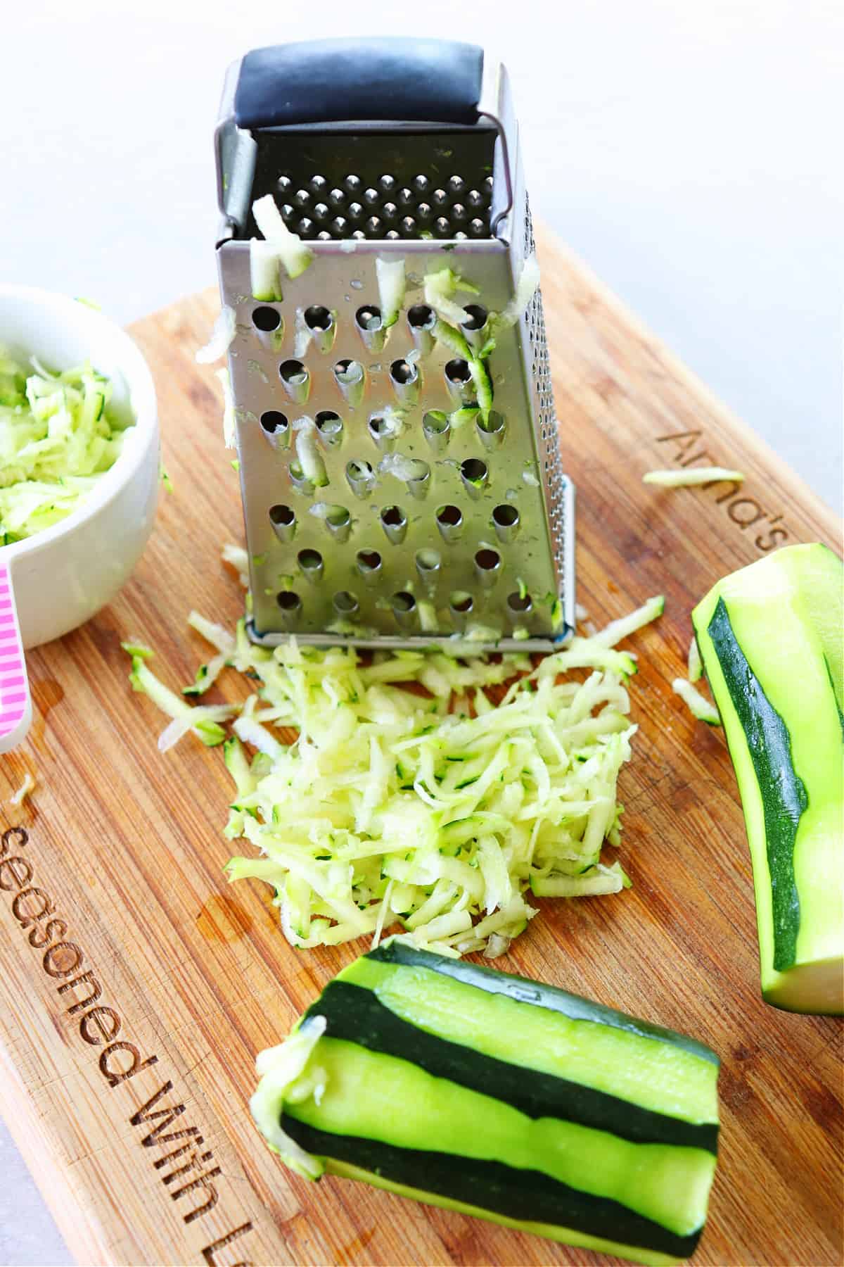Shredded zucchini with a grater box on a wooden cutting board.