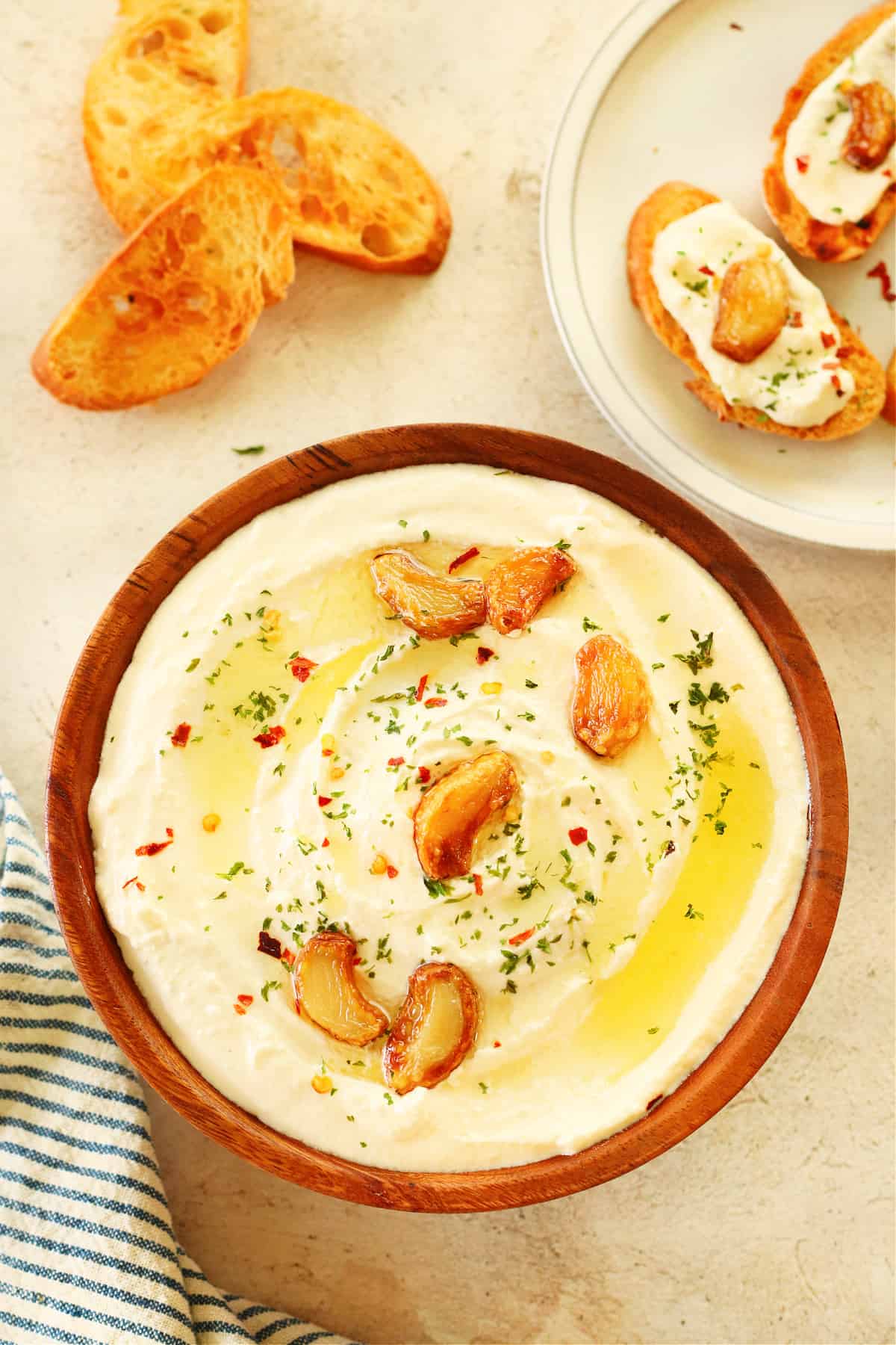 Feat dip with roasted garlic. Feta dip with garlic in a wooden bowl on cream board.