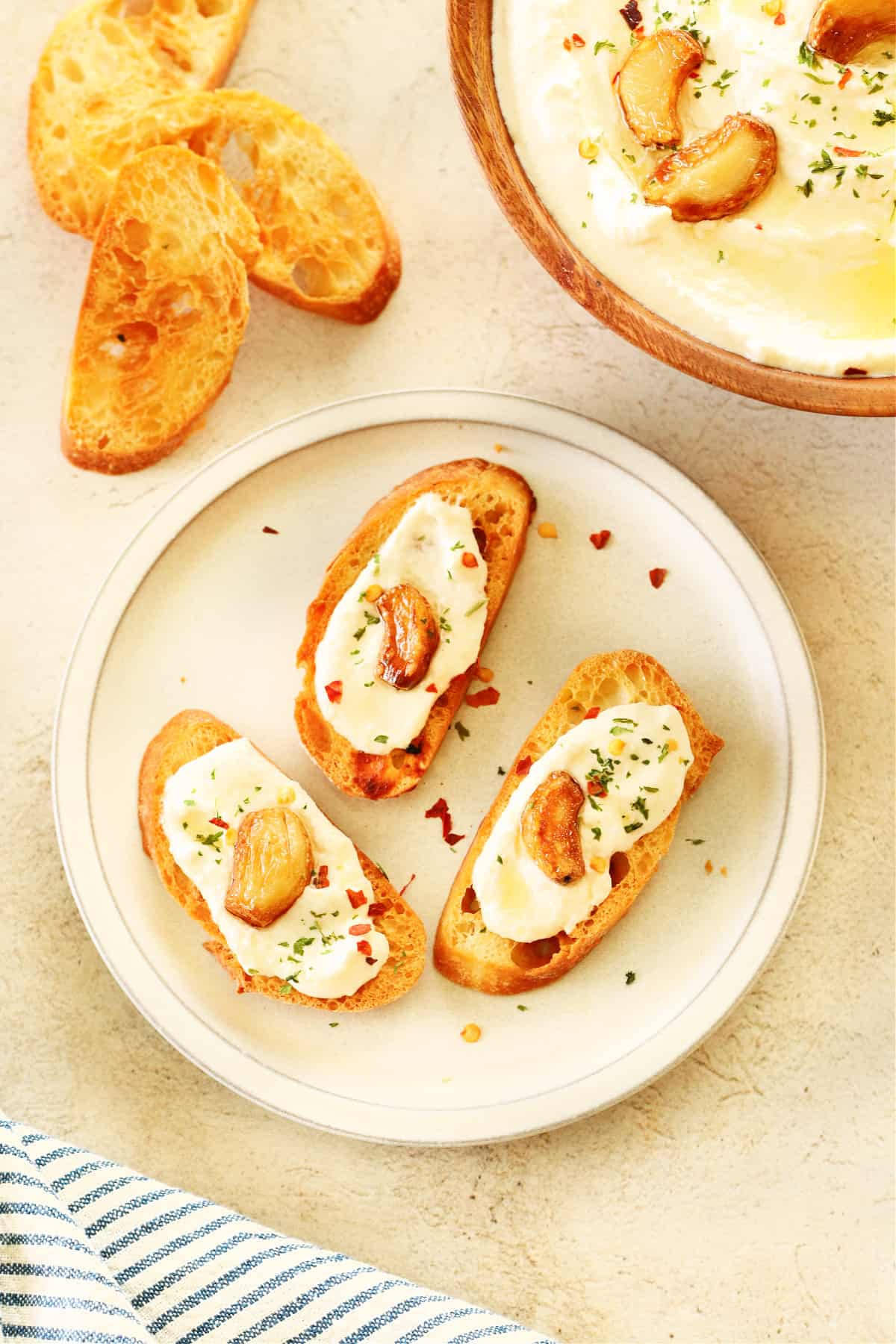 Three slices of baguette with feta dip and roasted garlic on a small plate.
