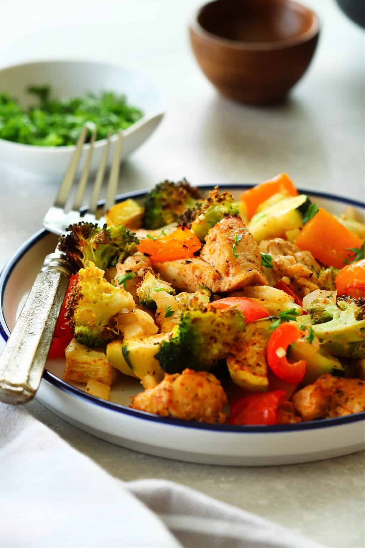 Side shot of chicken and veggies on a plate with blue rim and fork.