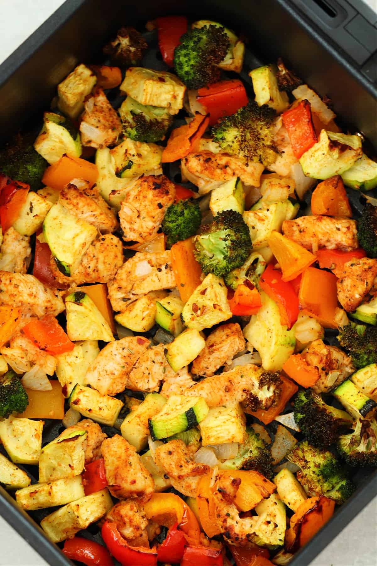 Cooked chicken and veggies in the air fryer basket.