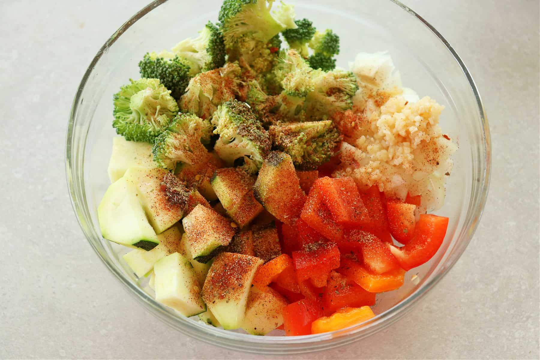 Chopped raw vegetables with seasoning in a glass bowl.