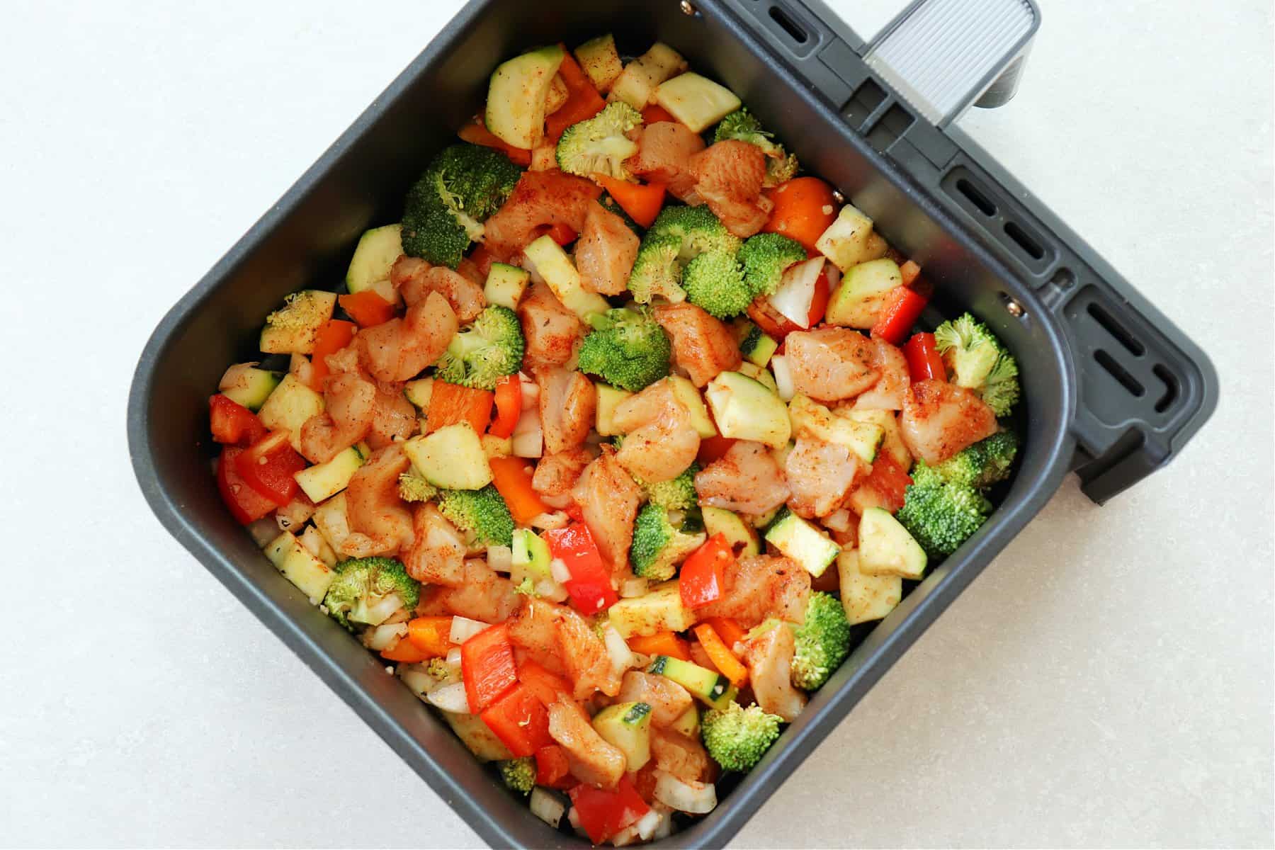 Raw chicken and vegetables in the air fryer basket.