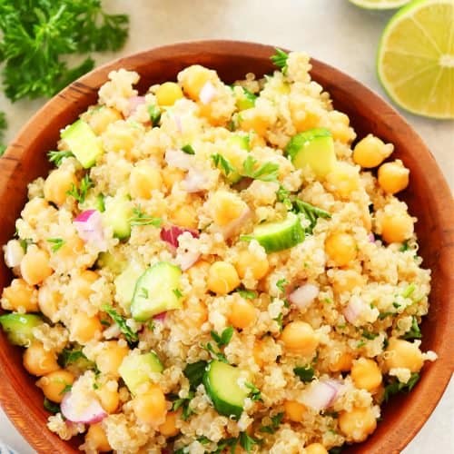 Quinoa salad with chickpeas and cucumber in a wooden bowl on cream background.