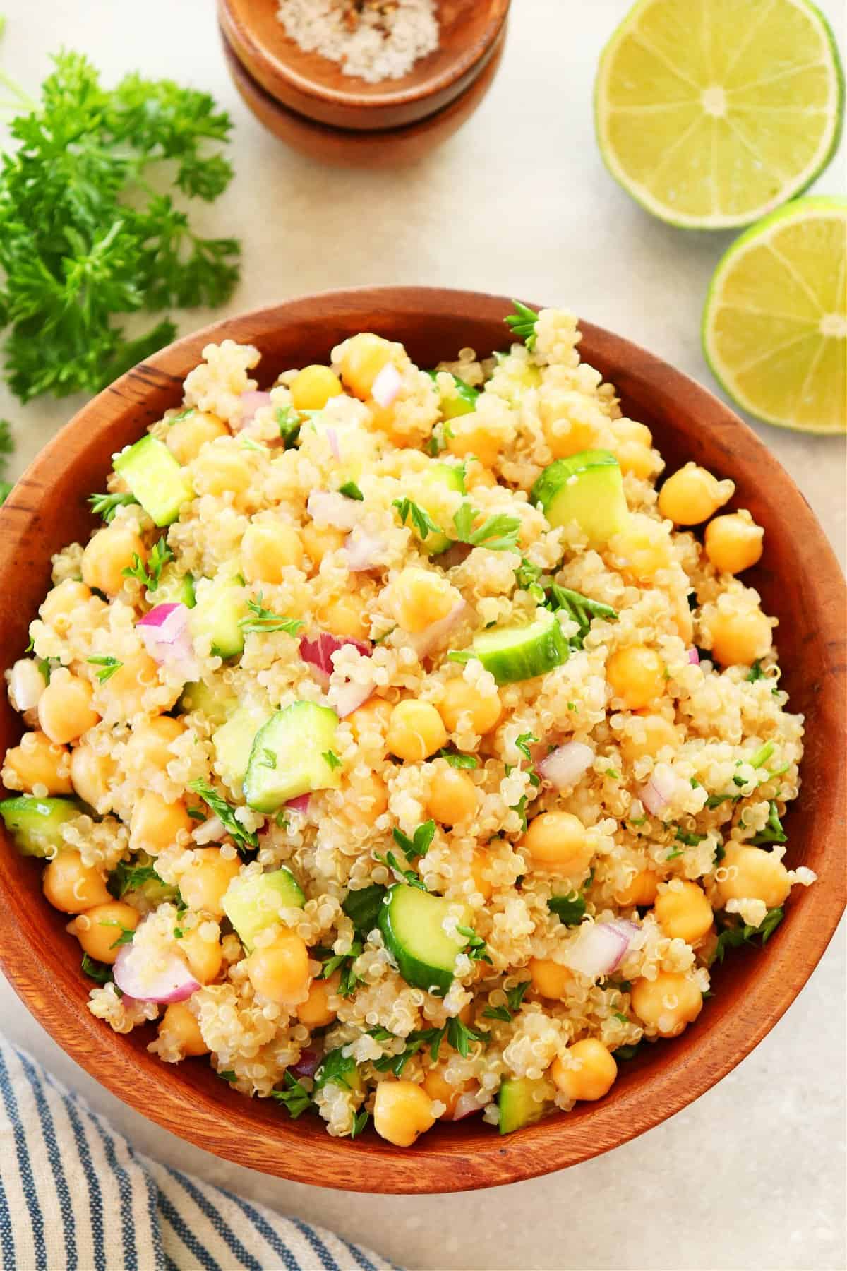 Quinoa salad with chickpeas and cucumber in a wooden bowl on cream background.