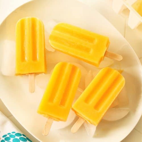 Mango popsicles on ice cubes on white plate.