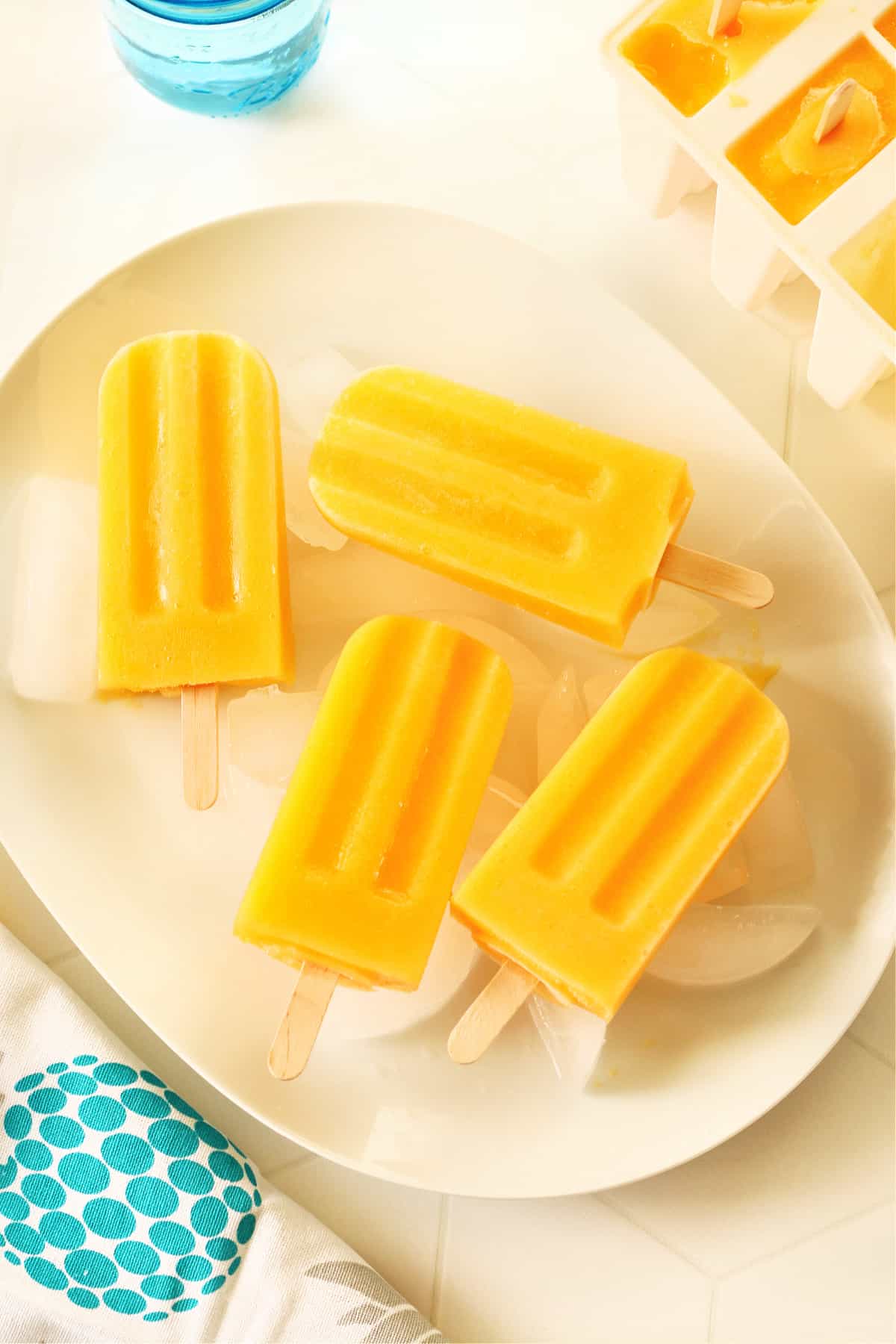 Mango popsicles on ice cubes on white plate.