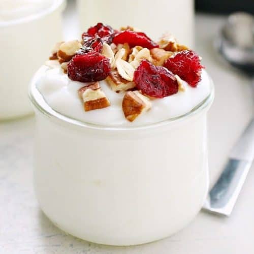 Yogurt in a small glass jar with dried cranberries and nuts on top.