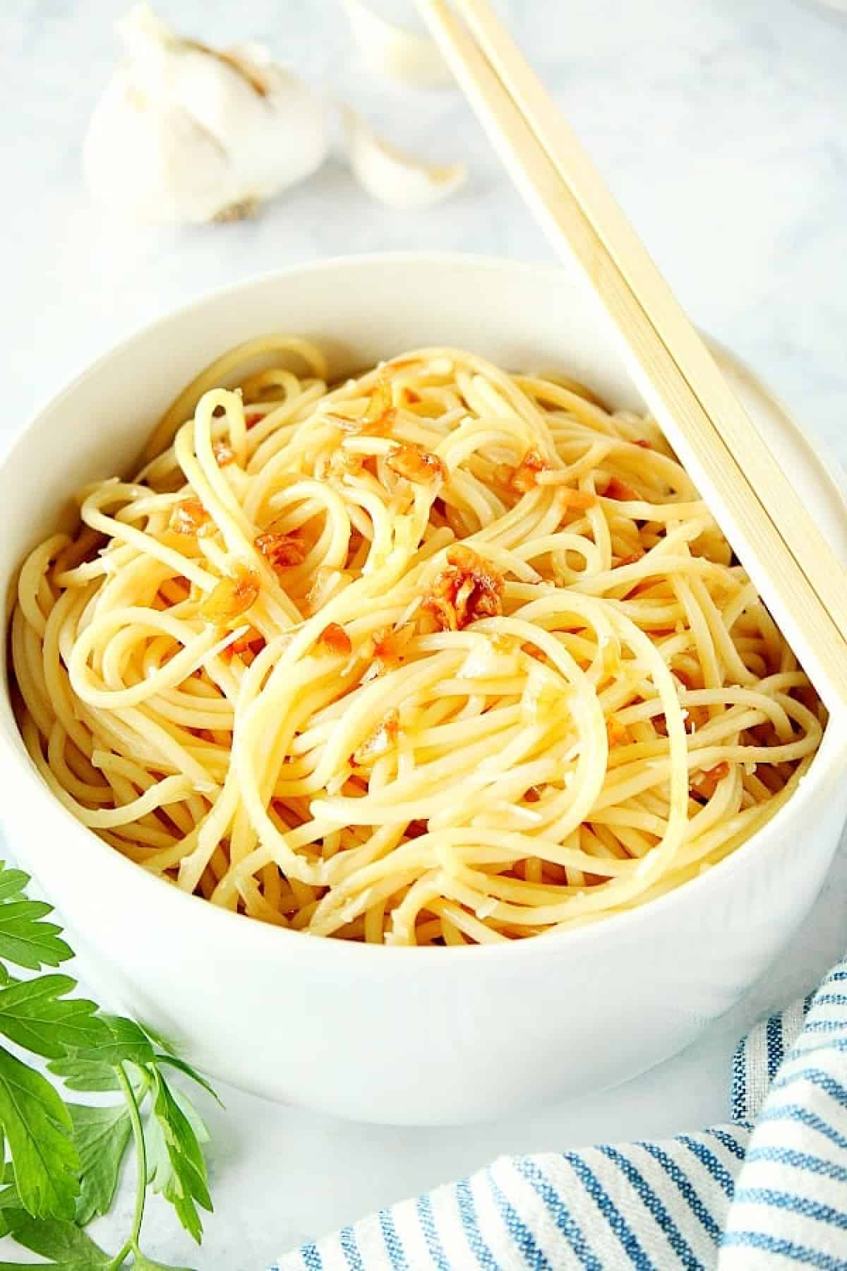 Noodles with garlic in a white bowl with chopsticks placed on the edge.