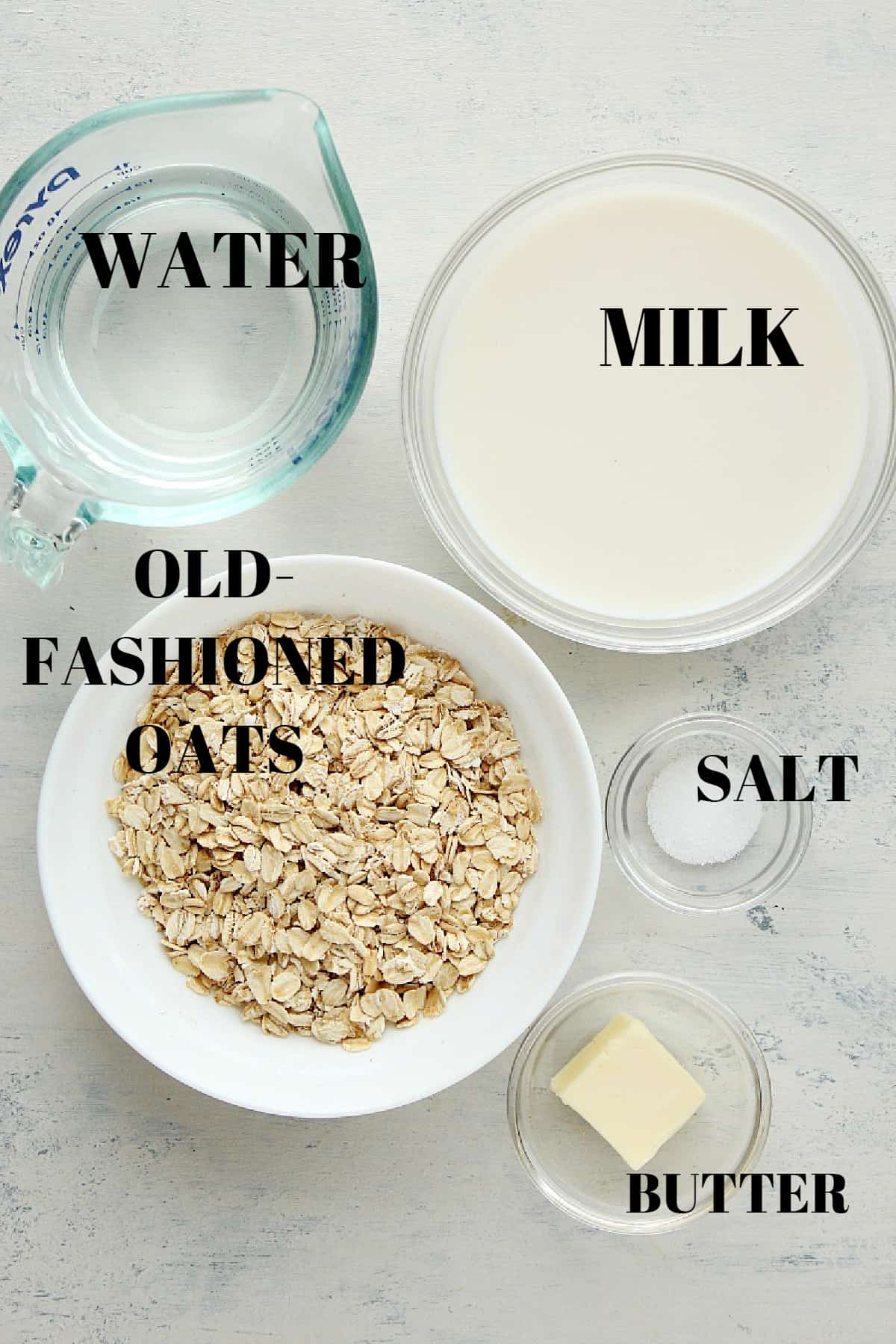 Oats, milk, water, salt and butter in small bowls, on a gray background.