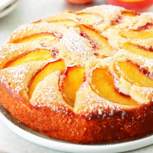 Square photo of a cake with peach slices and dusting of powdered sugar.
