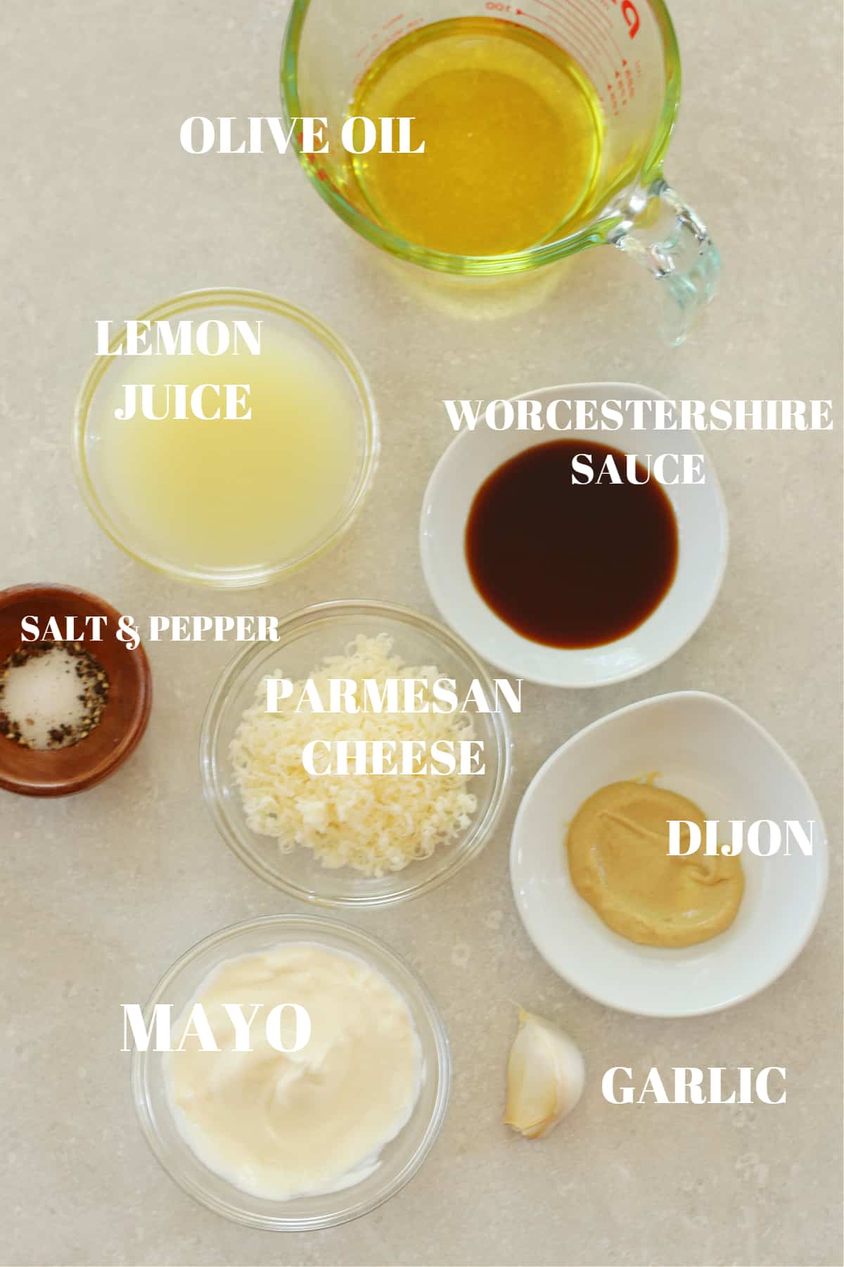 All ingredients for the Caesar salad dressing in small bowls, on a gray board.