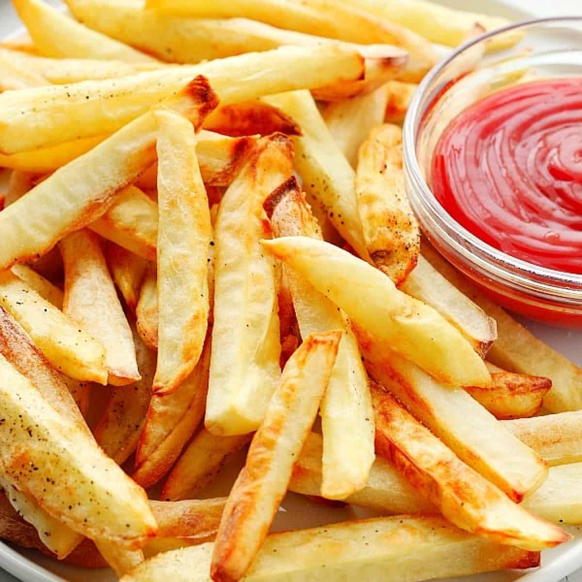 Square close up photo of air fried French fries on a plate with ketchup.