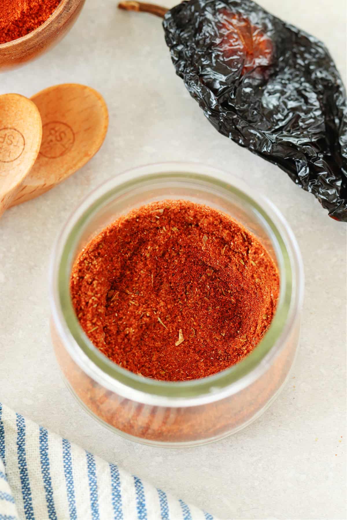 Close up photo of chili seasoning in a glass jar, on a gray board.