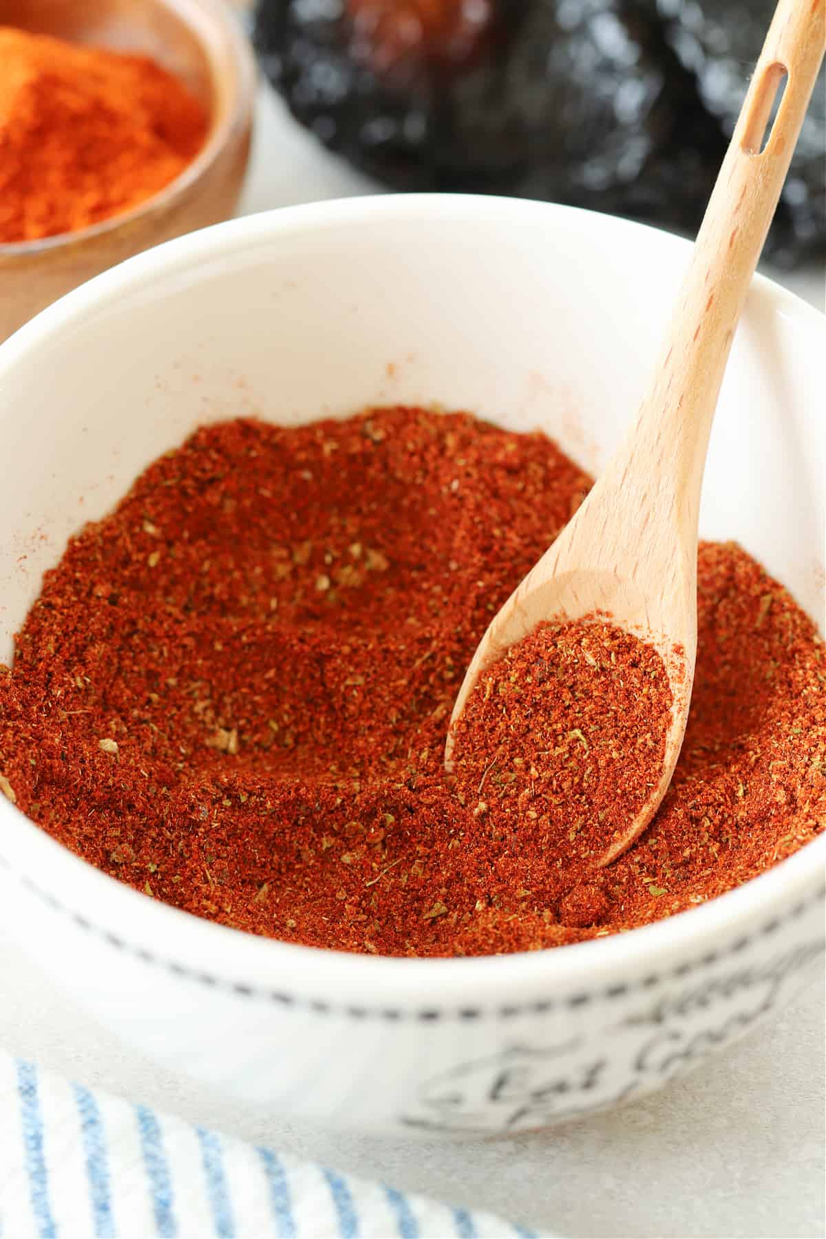 Chili seasoning in a white bowl with a small wooden spoon.