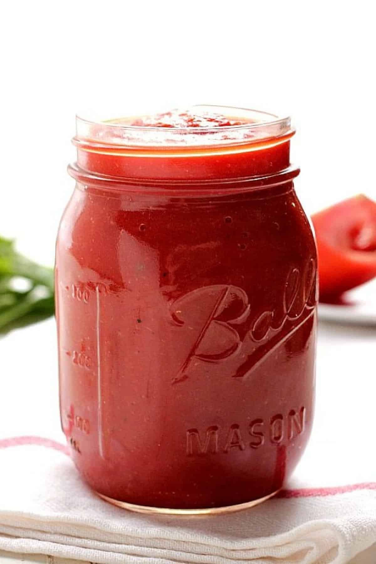 Pizza sauce in a glass jar on white kitchen towel.