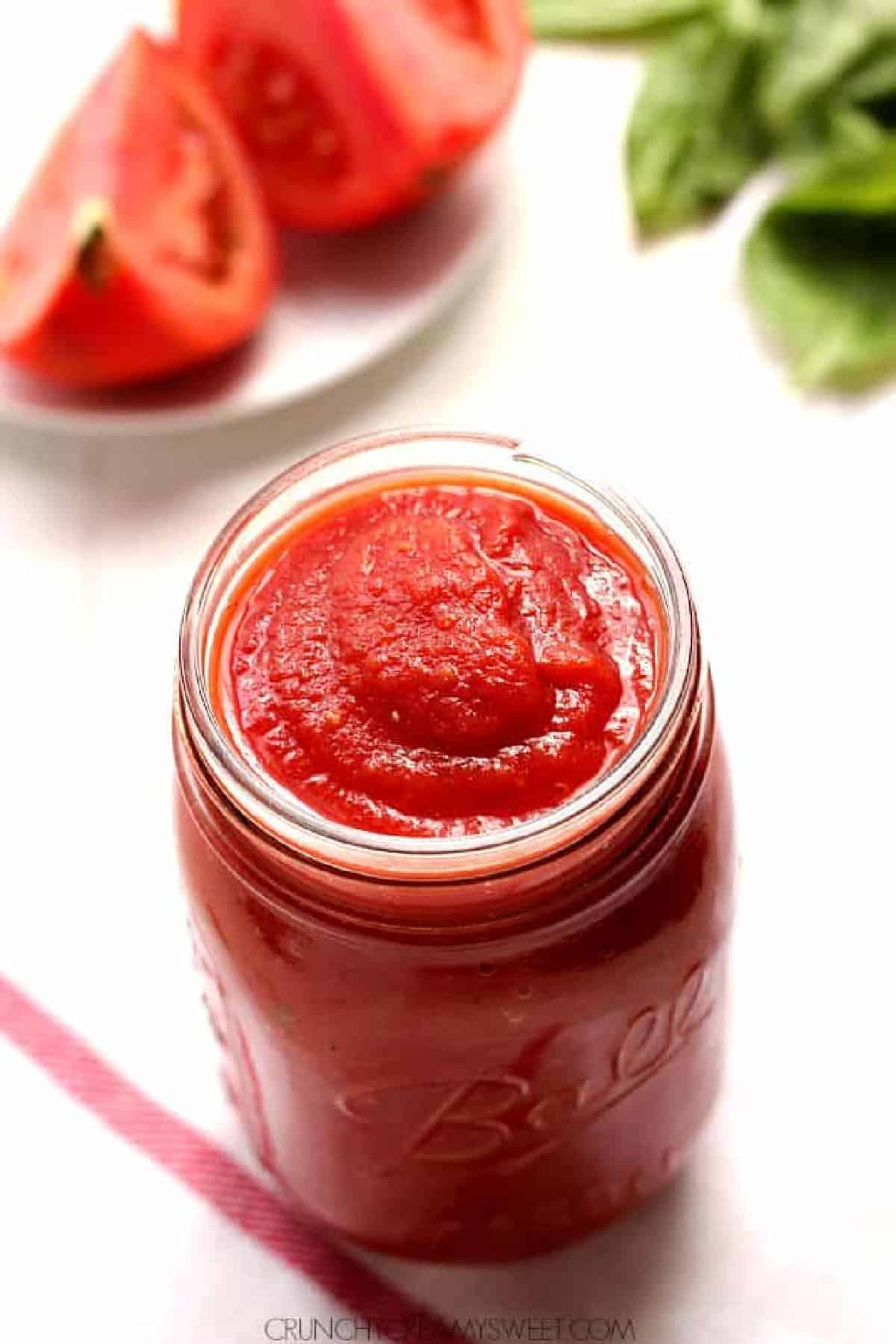 Tomato sauce in a glass jar on a white board.