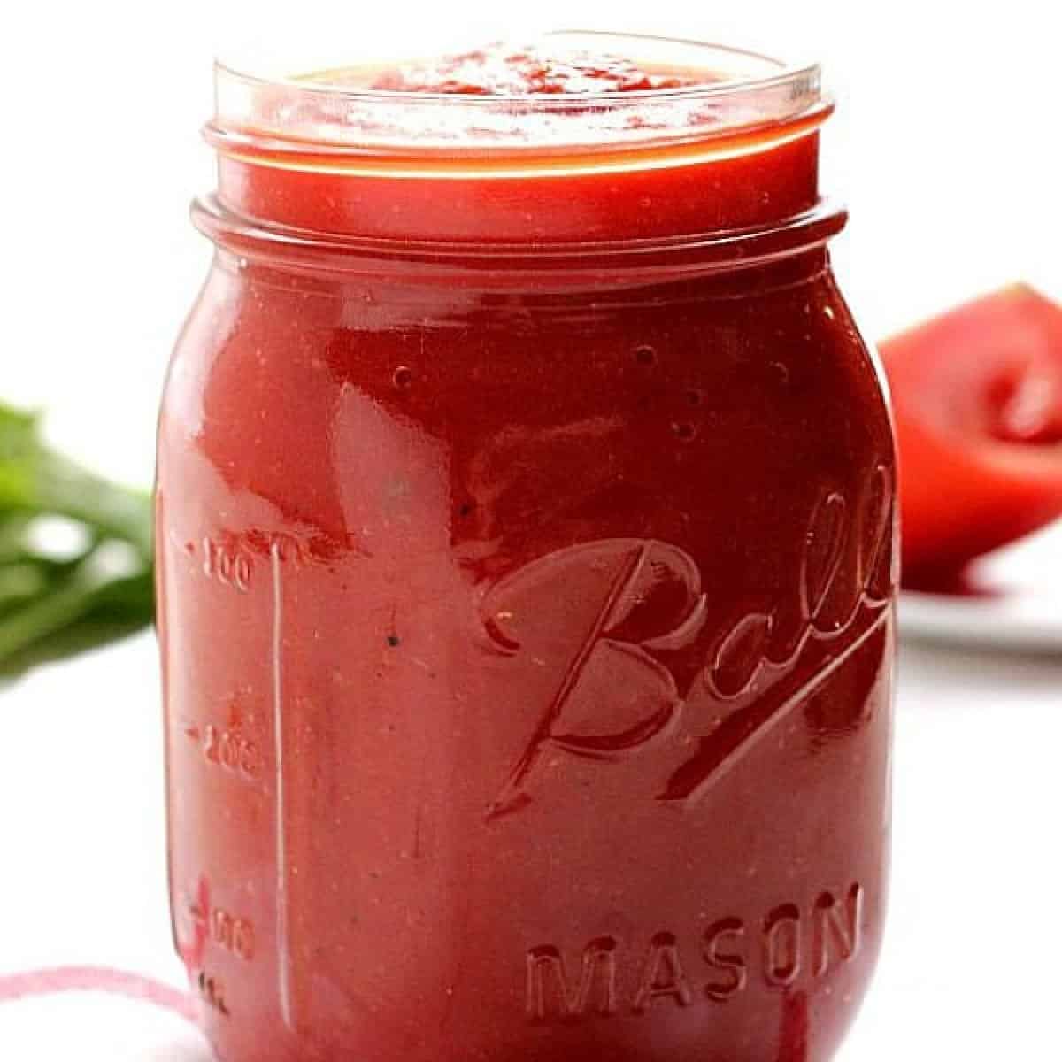 Square image of pizza sauce in a glass jar on white background.