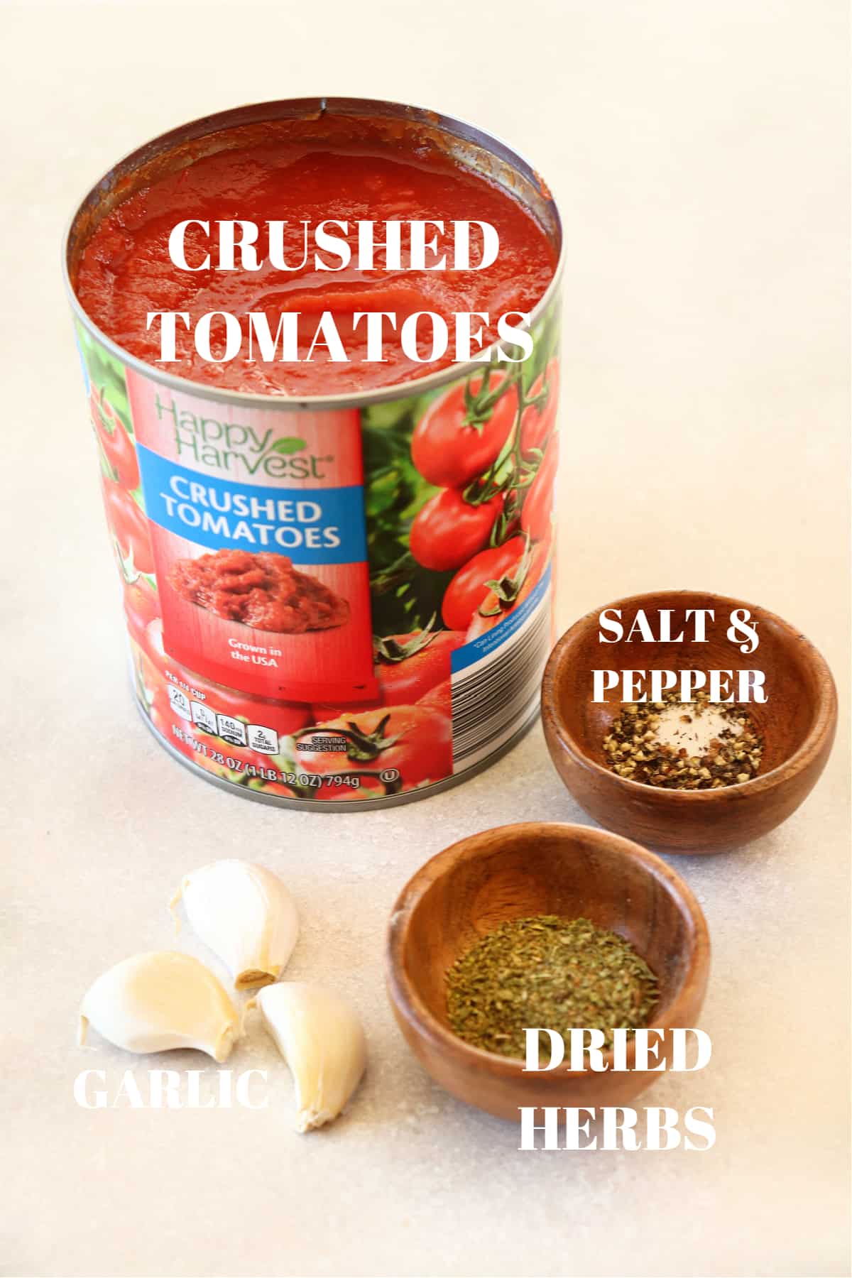 Can of crushed tomatoes, fresh garlic cloves and seasoning in small wooden bowls, all set on a gray board.
