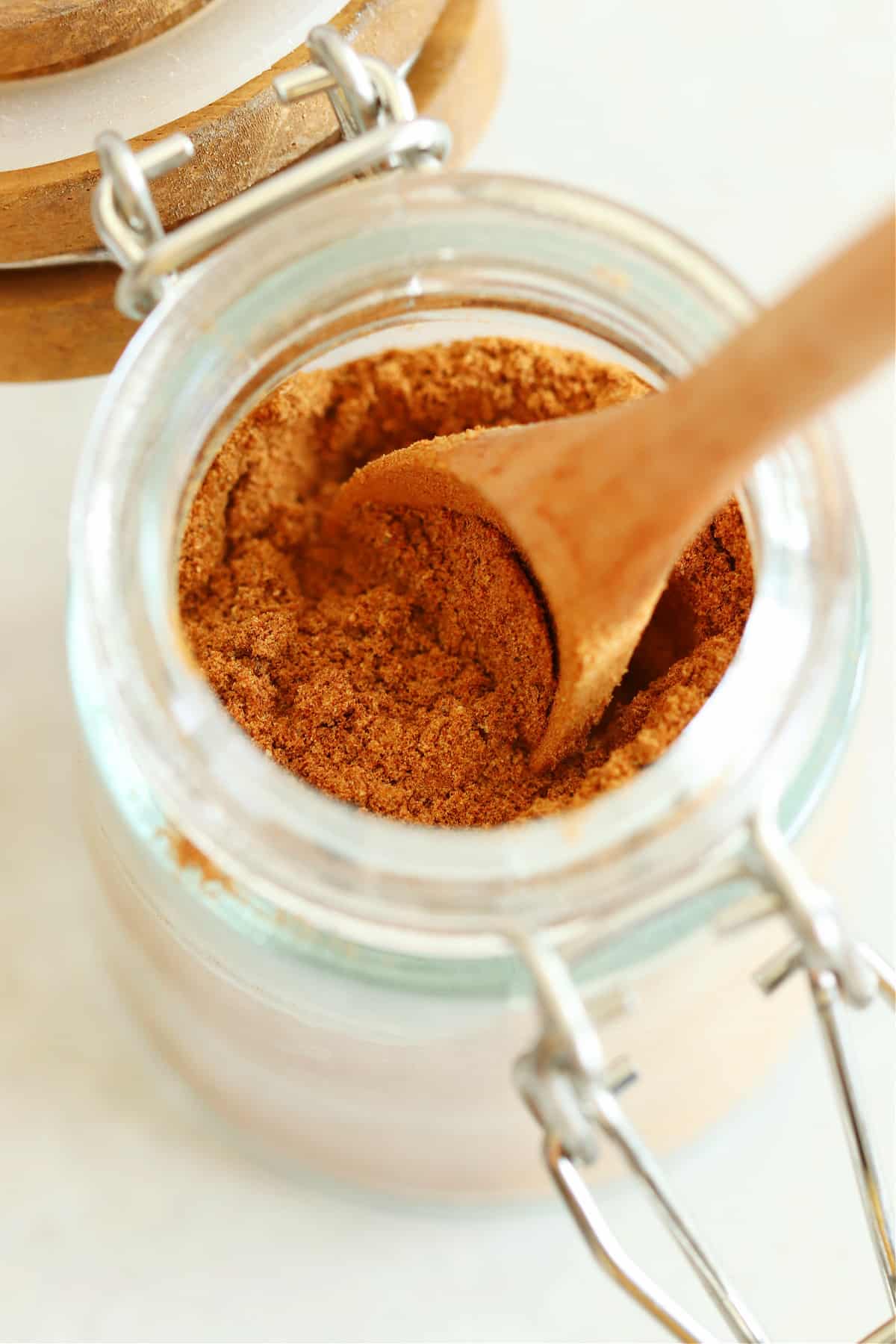 Close up photo of pumpkin pie spice in a glass jar with a wooden spoon inside.