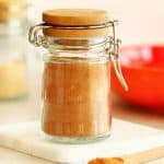 Pumpkin pie spice mix in a small spice jar with hinge top, set on a marble coaster, with a wooden spoon infront of it.