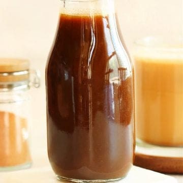 Pumpkin syrup in a glass bottle on a marble coaster.