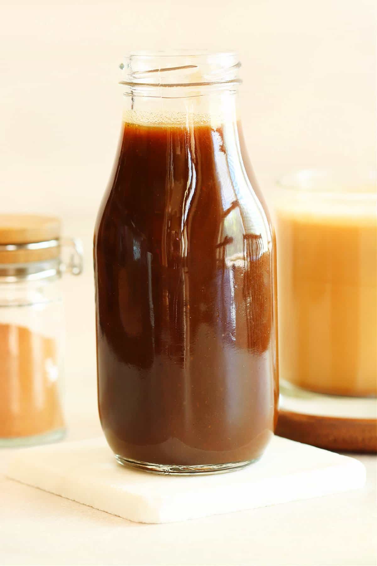 Pumpkin syrup in a glass bottle on a marble coaster.