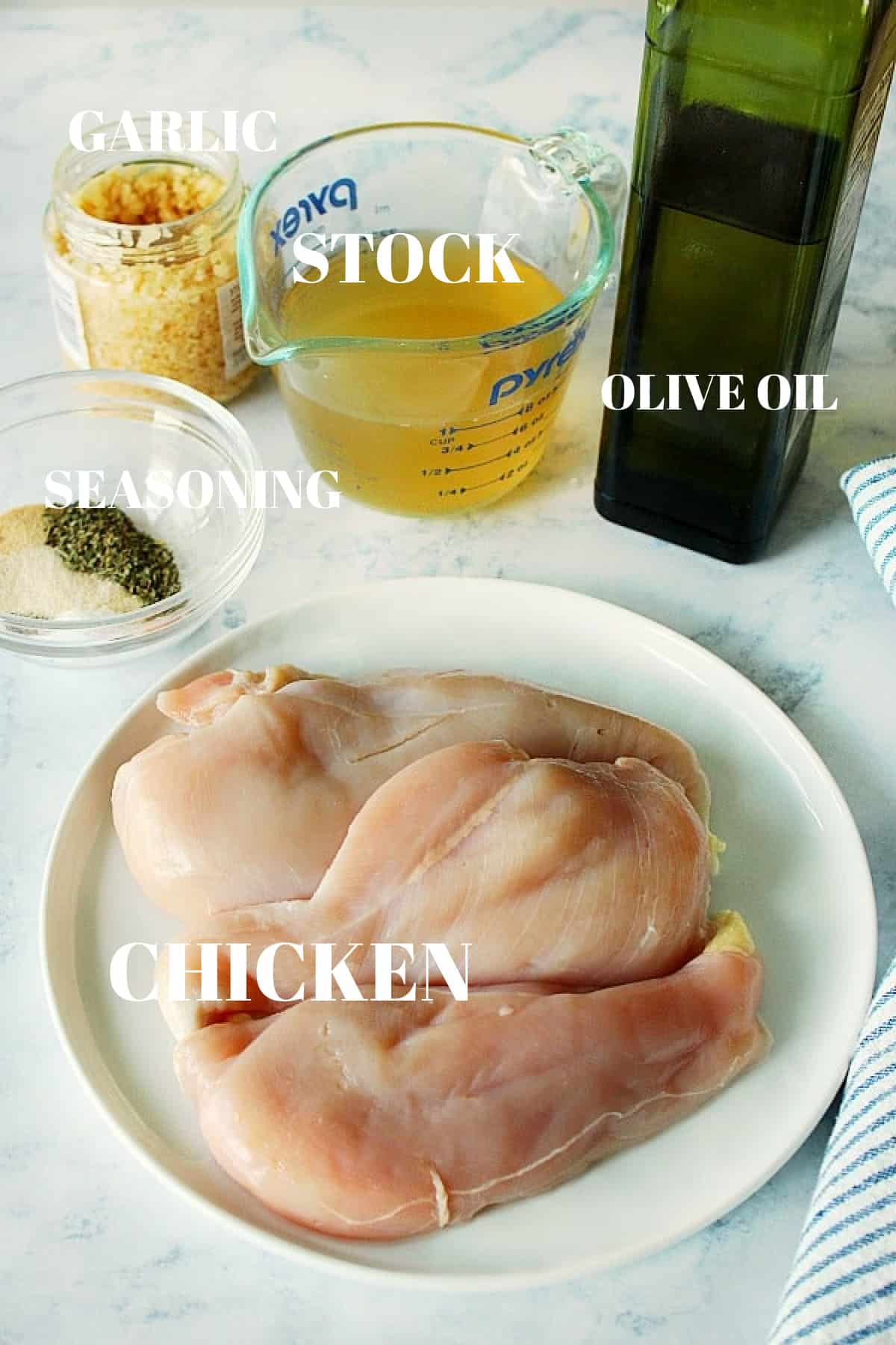 Chicken breasts, olive oil, stock, garlic and seasoning on a marble board.