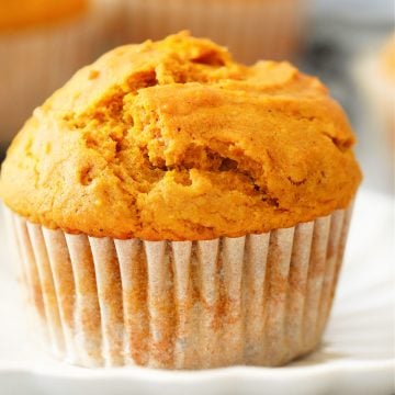 Close up photo of a pumpkin muffin in parchment liner on a white dessert plate.