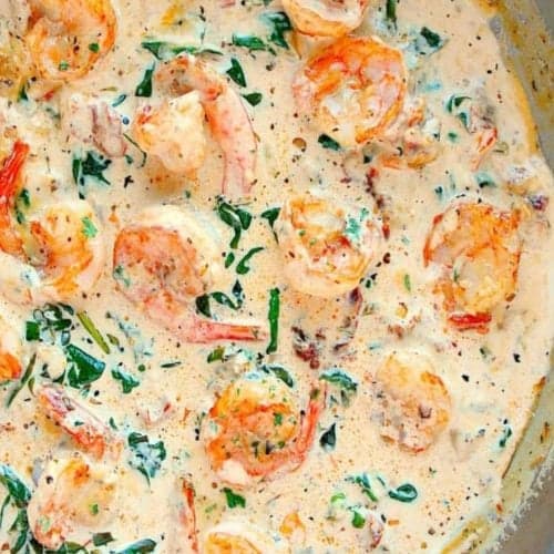 Square image of shrimp in creamy Tuscan sauce in stainless steel pan.