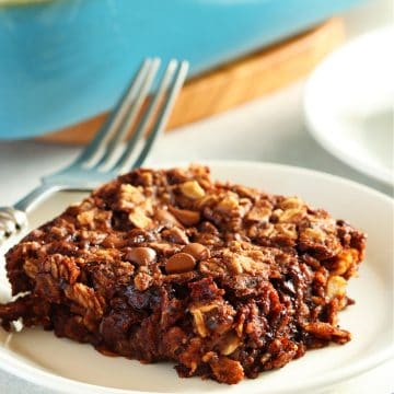 One serving of baked chocolate oatmeal on a small white plate with the baking dish in the background.