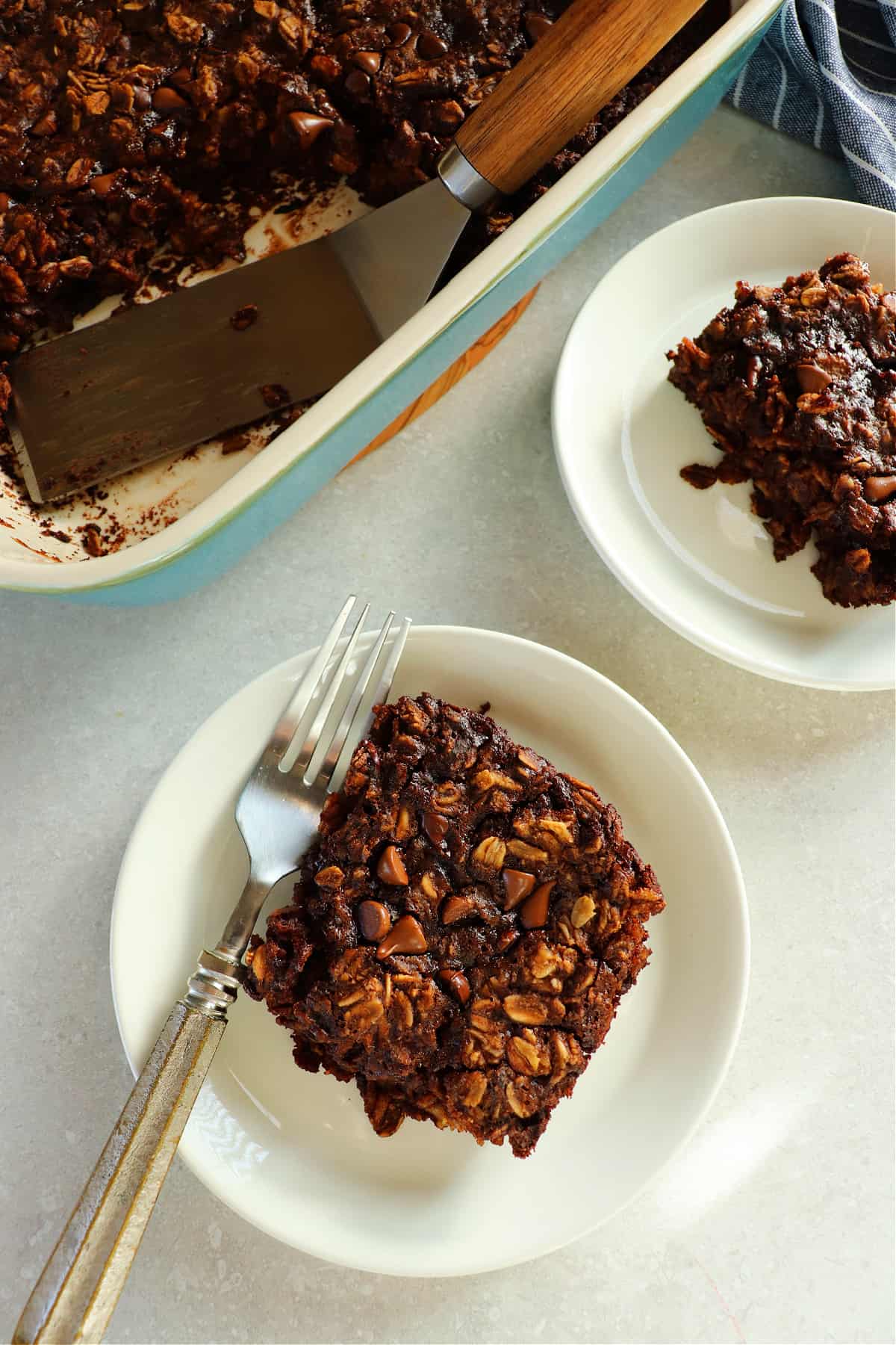 Overhead photo of two serving of baked chocolate oatmeal on small white plates and in the baking dish.