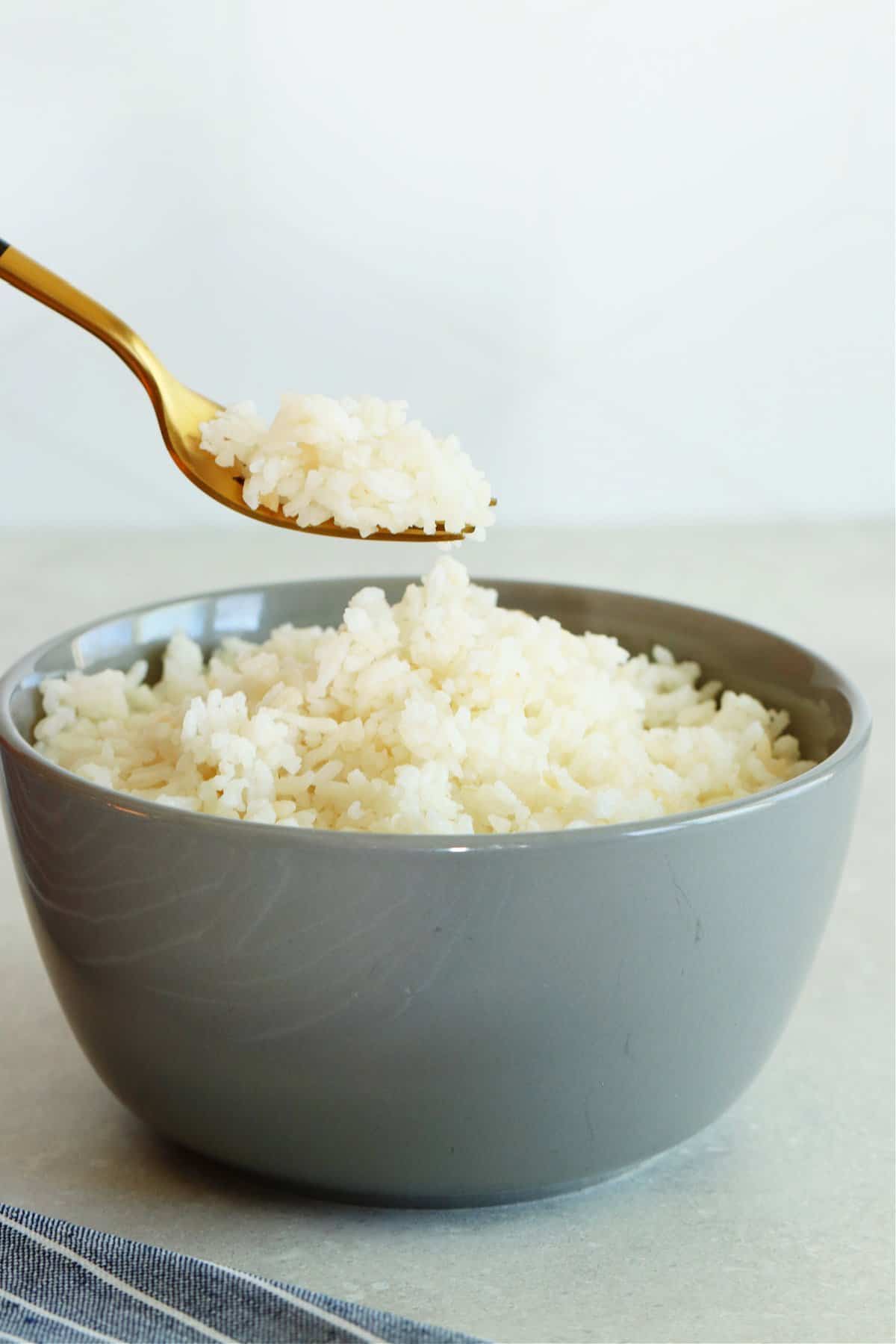 Gray bowl with rice and fork above it with rice on it.