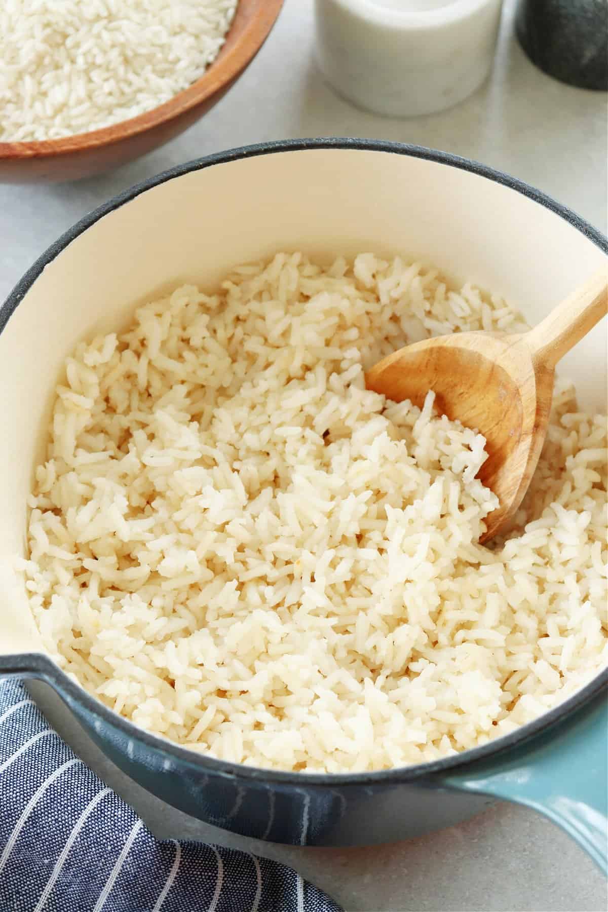 Cooked white rice in a saucepan with wooden spoon inside.