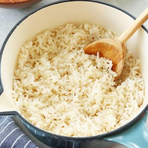 Square image of cooked long-grain rice in a blue pot on a gray board.
