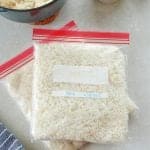 Cooked rice in freezer bags on a gray board with dried rice in a wooden bowl.