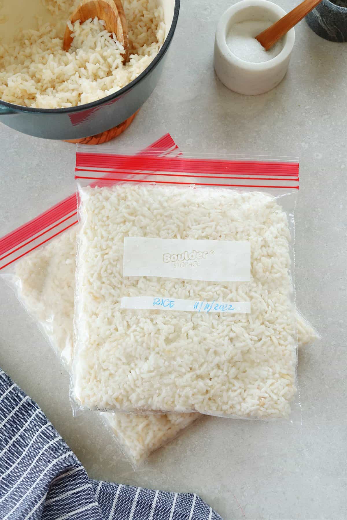 Cooked rice in freezer bags on a gray board with dried rice in a wooden bowl.