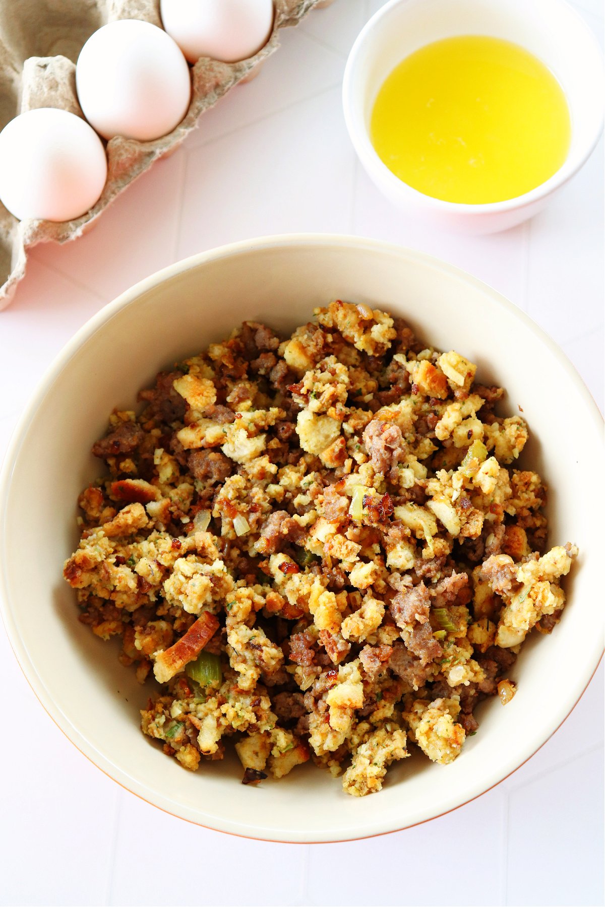 Stuffing in a bowl, melted butter in a small bowl and eggs in a carton on a white board.