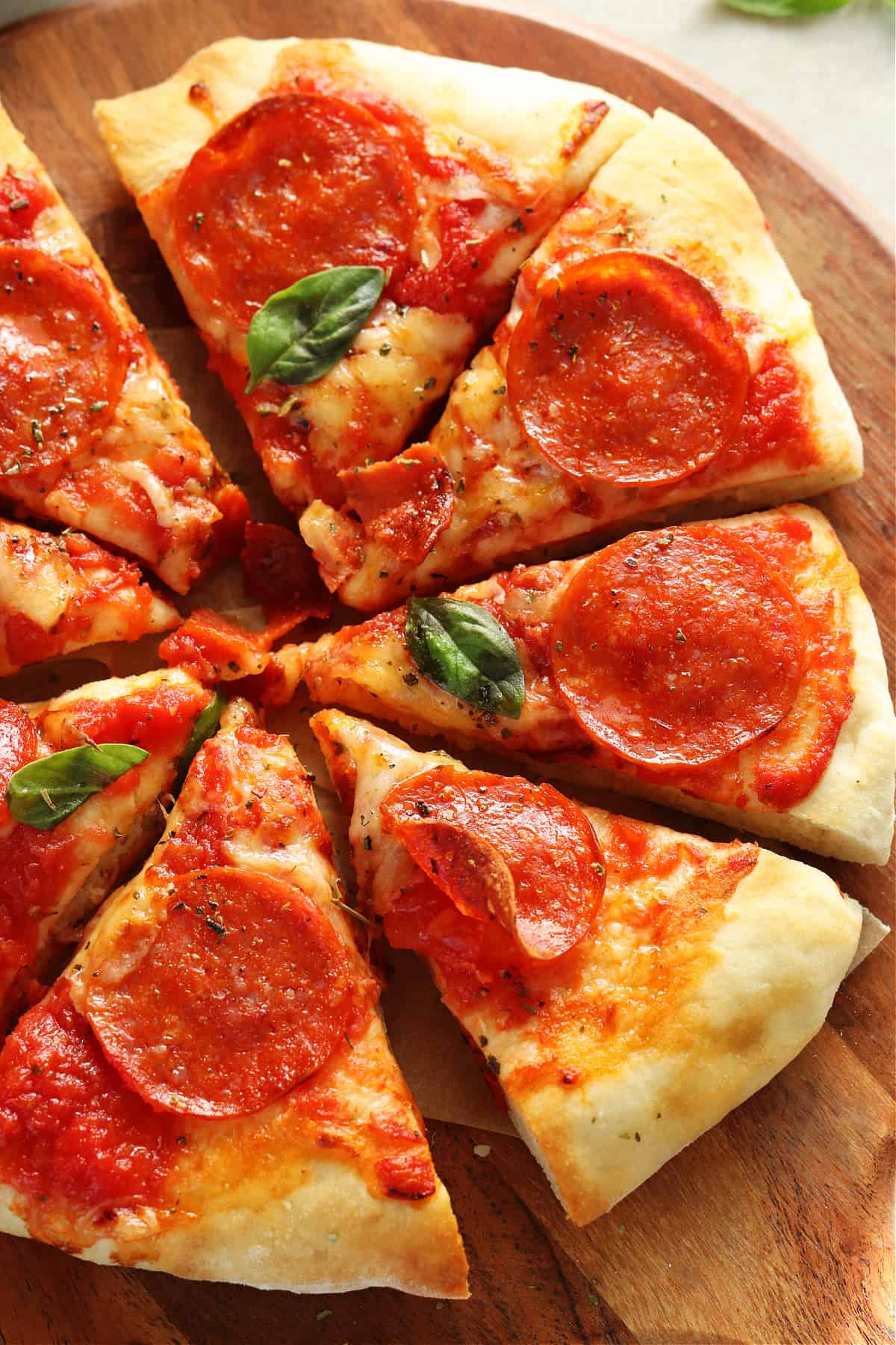 Sliced pizza on a round wooden cutting board.