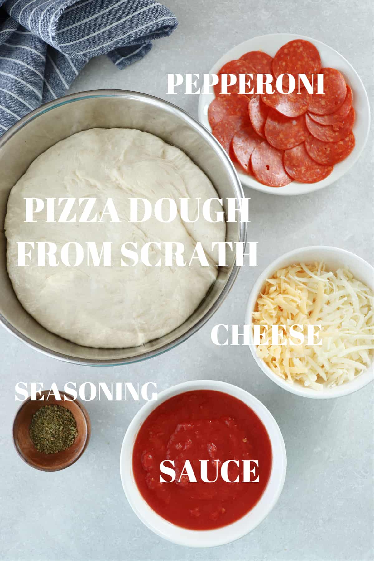 Pizza dough, tomato sauce, cheese, pepperoni and seasoning in bowls on a gray board.