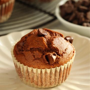 Chocolate muffin in a wrapper on a small plate with more muffins behind it.