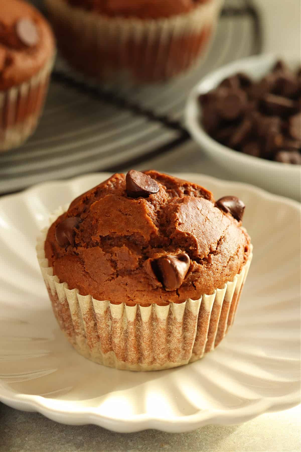 Muffin al cioccolato in un involucro su un piattino con più muffin dietro.