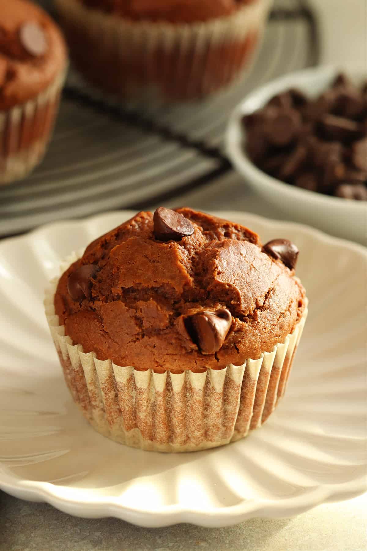 Chocolate muffin in a wrapper on a small plate with more muffins behind it.