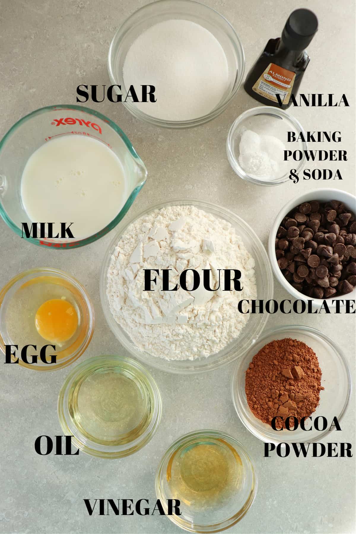 All ingredients for making chocolate muffins in small glass bowls on a gray board.