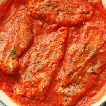 Overhead image of four chicken breasts in a tomato sauce in a skillet.
